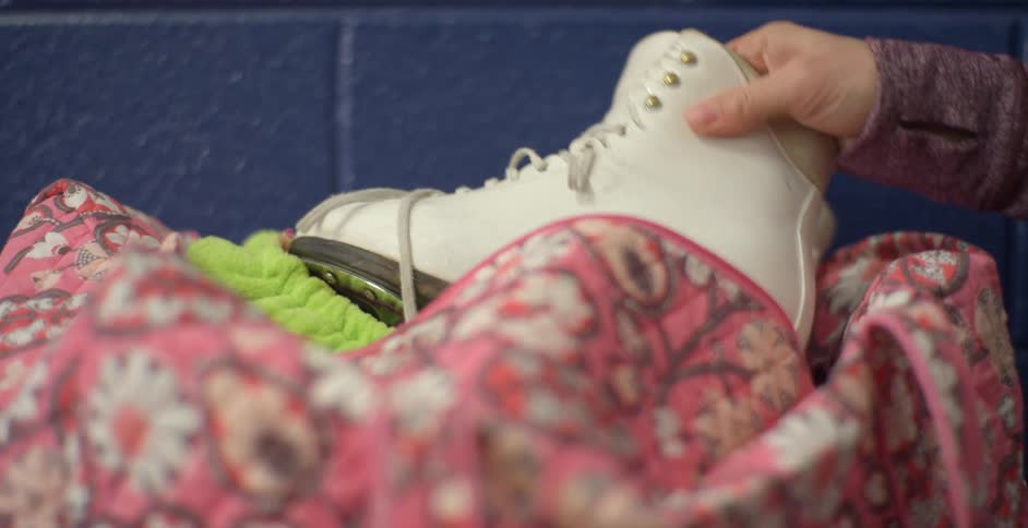 A hand reaches over and picks up a white ice skate with a green quilted guard on the blade