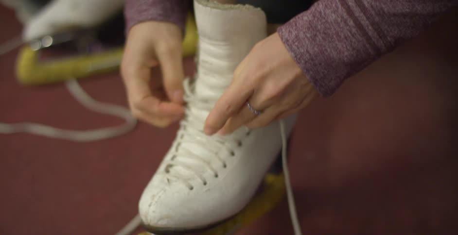A woman adjusts the shoe strings on her ice skate