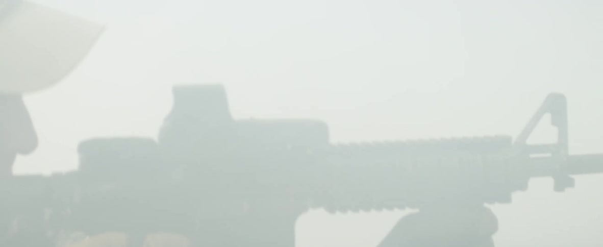 A person with a hat in smoke pointing a rifle