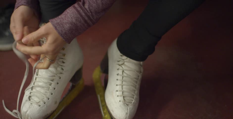 Female tightens the laces on her ice skate as she places each string into the hook of the boot