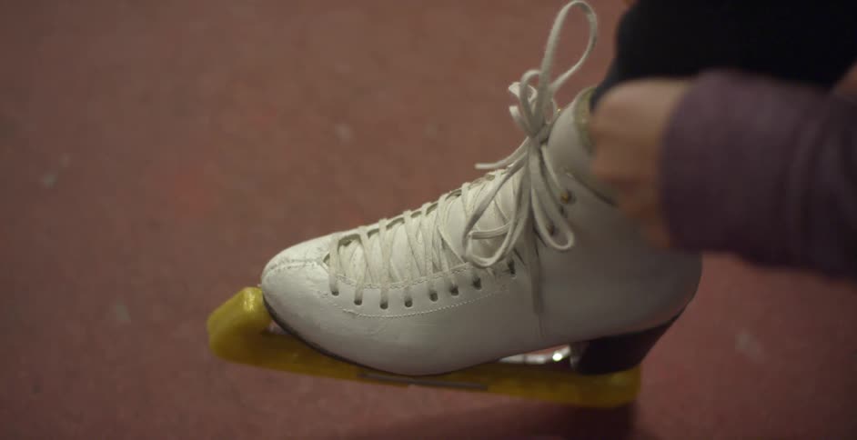 A woman ties the strings on her ice skates and adjusts the leg of her pants
