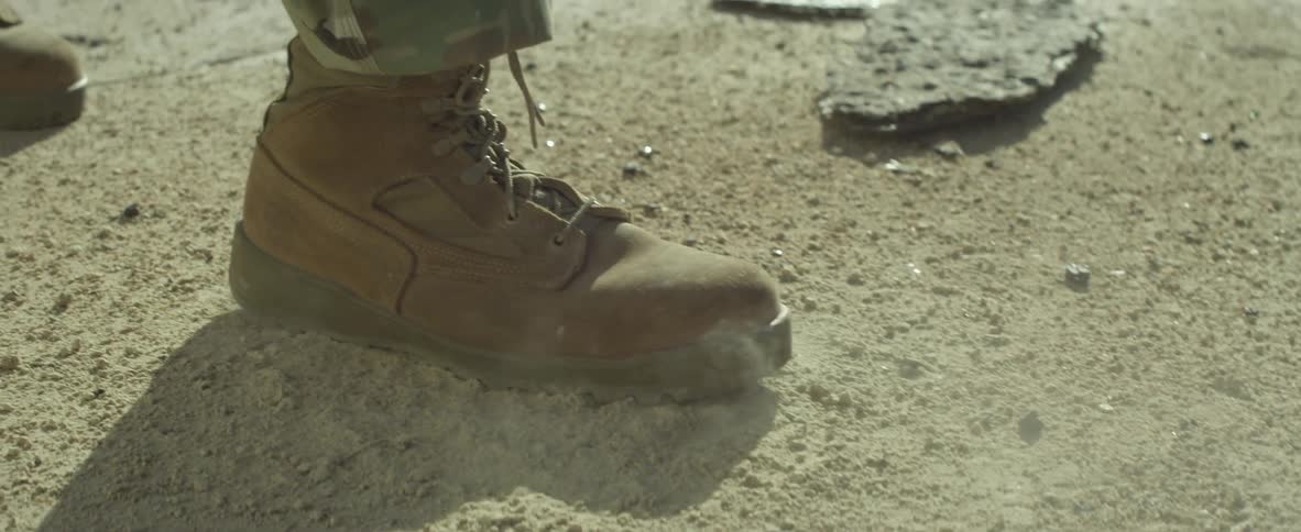 A leather boot stomps on the ground and kicks up a dust cloud