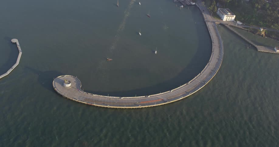 Long curved pier sits in the river as boats travel nearby