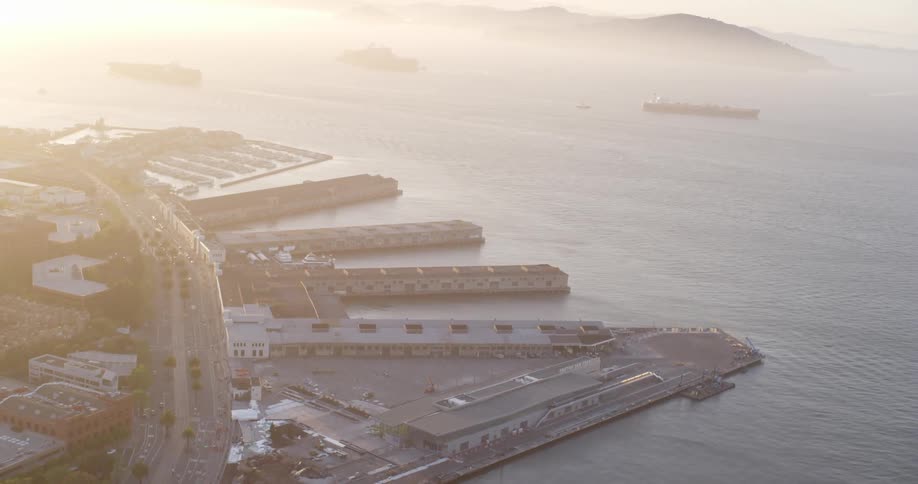 Large barges and shipping boats sit off the coast near a port