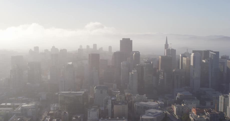 Sunlight peaks through fog that covers a dense city