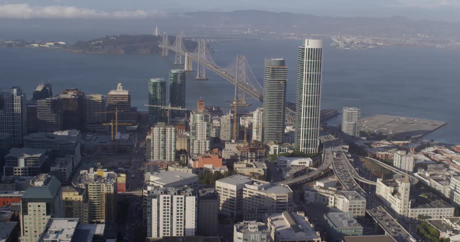 Buildings in a city sit next to the river while traffic travels on the bridge
