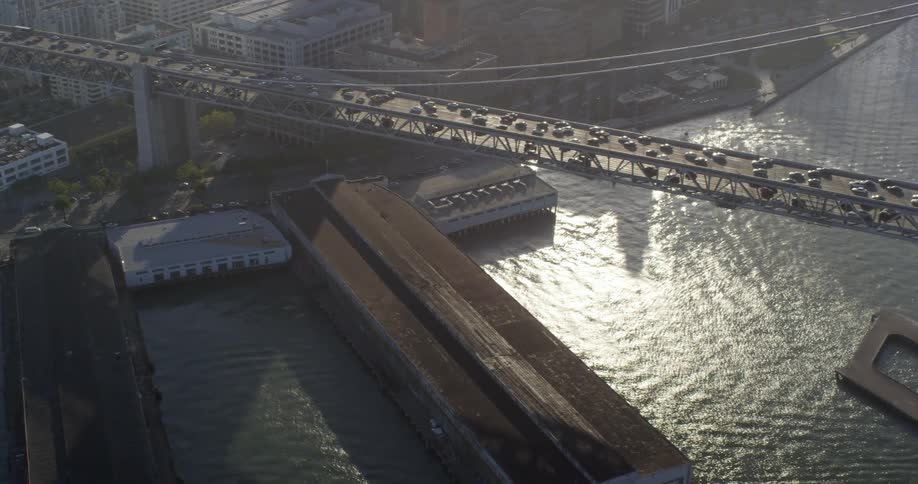 An aerial view of a citys waterway with traffic moving over a large suspension bridge at dusk