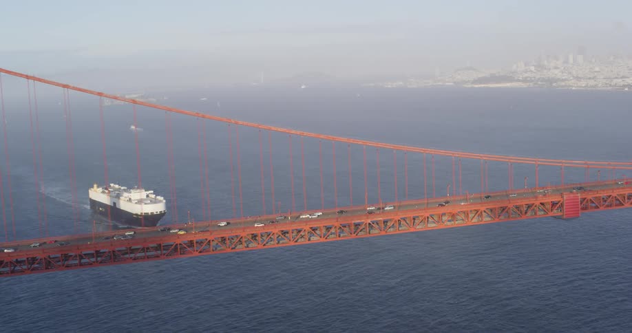 A large boat about to pass under a bridge with cars driving over it