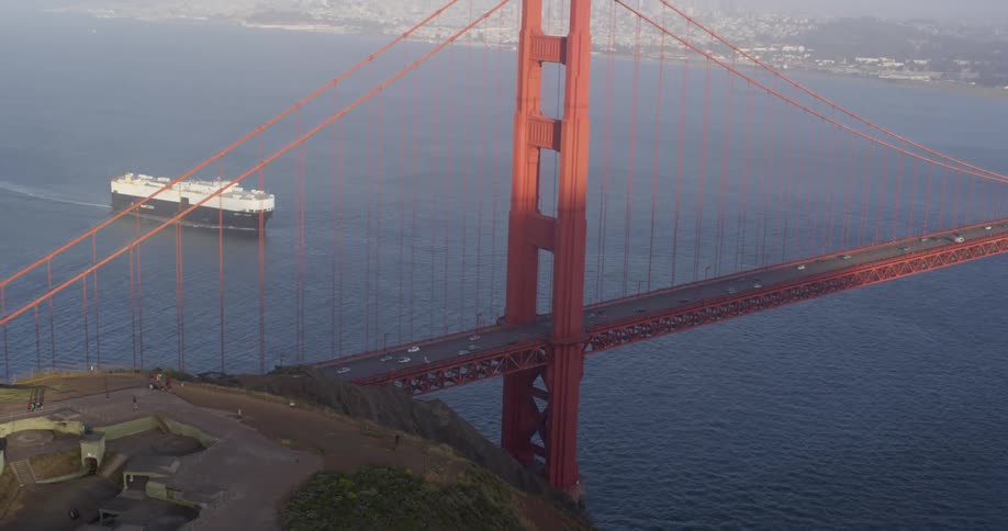 The golden gate bridge with vehicles with the ocean a ship and the coast in the background