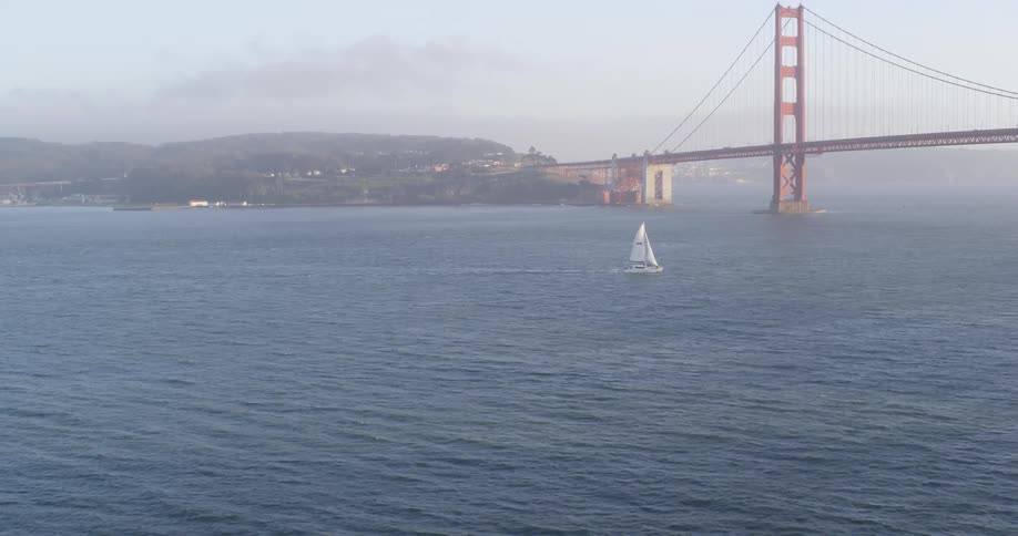 A sailboat moves through the water in front of the golden gate bridge