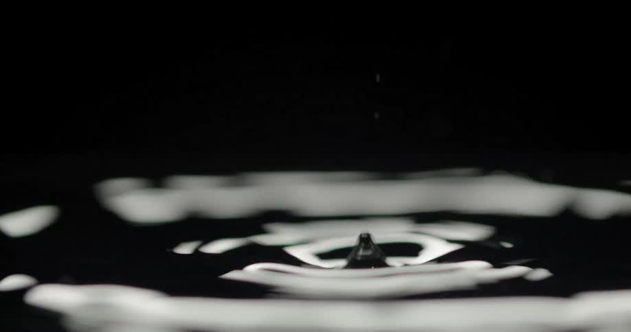 Water drops hit liquid surface causing ripples and small splash