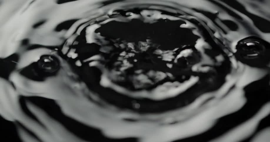 Drops hit surface of liquid creating bubbles and concentric circles of ripples