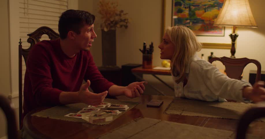 Husband and wife sitting face to face at the dining room table as they point and argue with one another