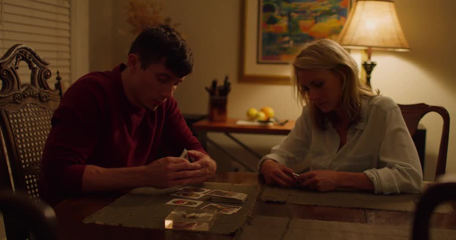 A white woman walks into a room and sits down at a dining table with a white man