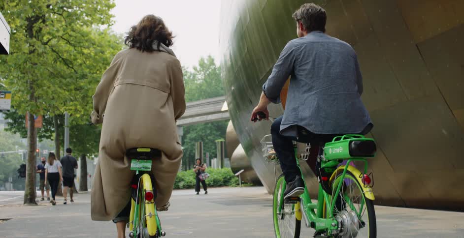 A man and woman bike side by side on a city plaza on rented bicycles