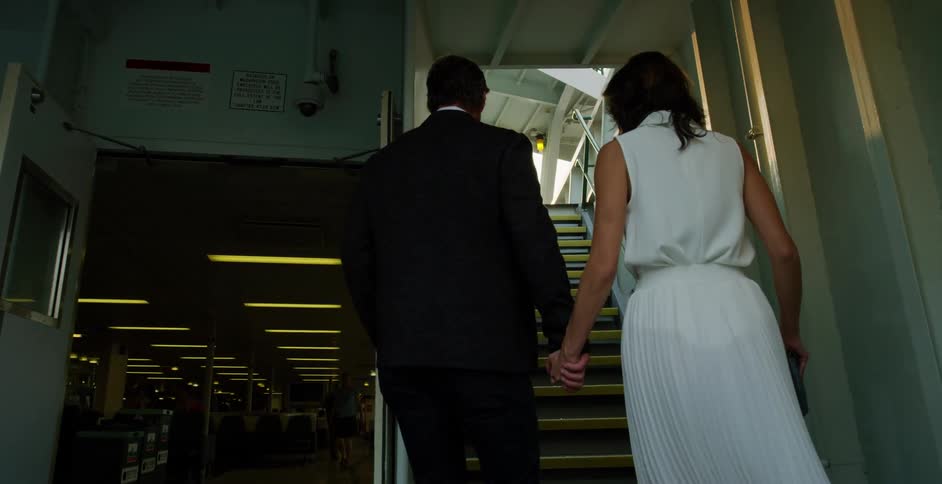 Couple holding hands walking towards stairs in a corridor