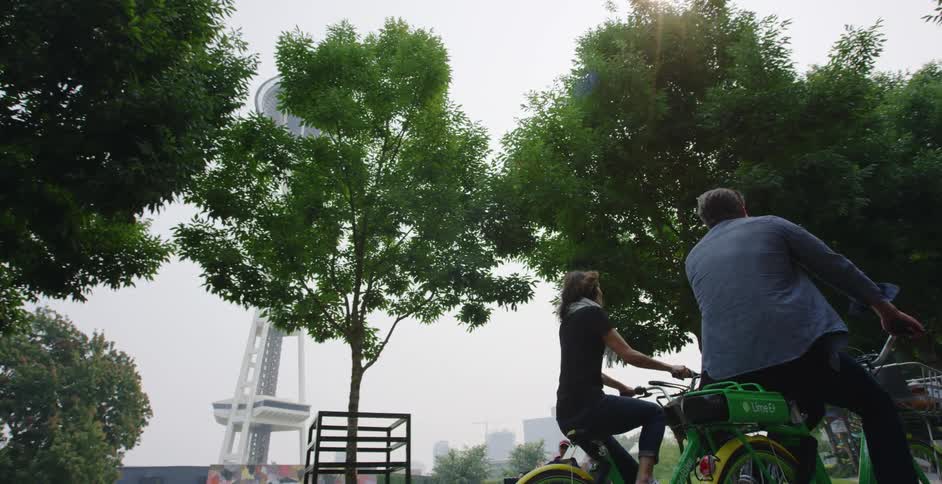 Male and female riding rental bicycles together around the park near the space needle tower