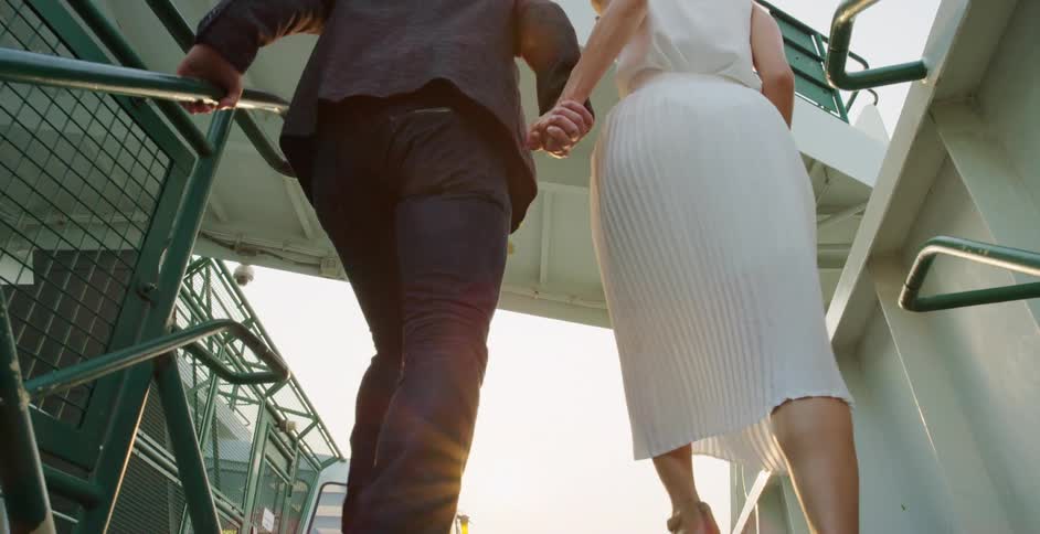 Woman and man in formal dress climb up the stairs holding hands at sunset