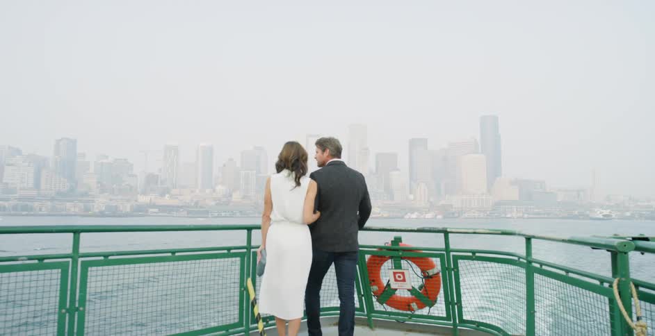 A man and woman standing on a boat arm in arm look at the city skyline