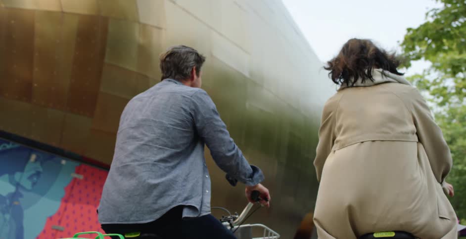 Couple rides bicycles down sidewalk near pedestrians