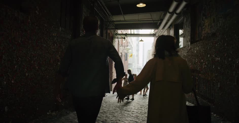 A man and woman hold hands walking down the alley