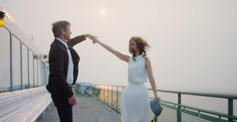 A newlywed husband and wife dance as they stand near the railing on a ferry in the ocean