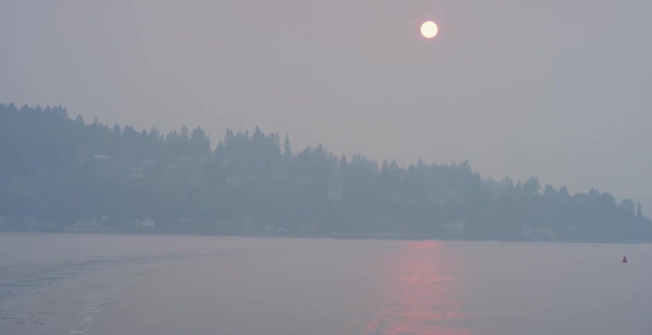 Coastal town covered in fog at sunset under a red sun