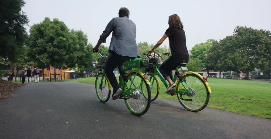 A man and a woman ride bicycles on a park path