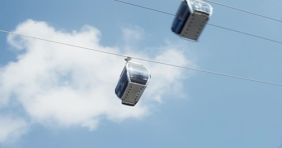 Overhead cable cars pass each other as they traverse cables under clouds