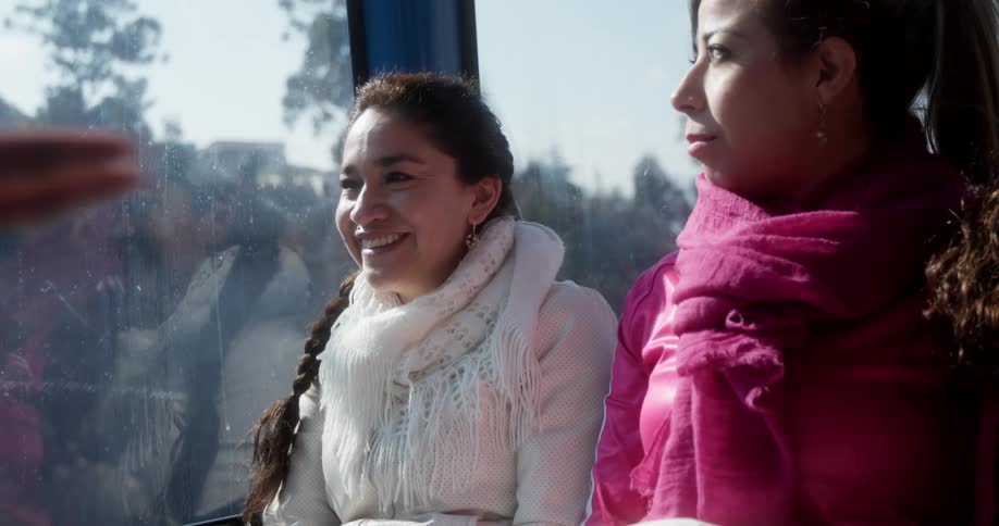 Two young women sitting on a bus talking and laughing