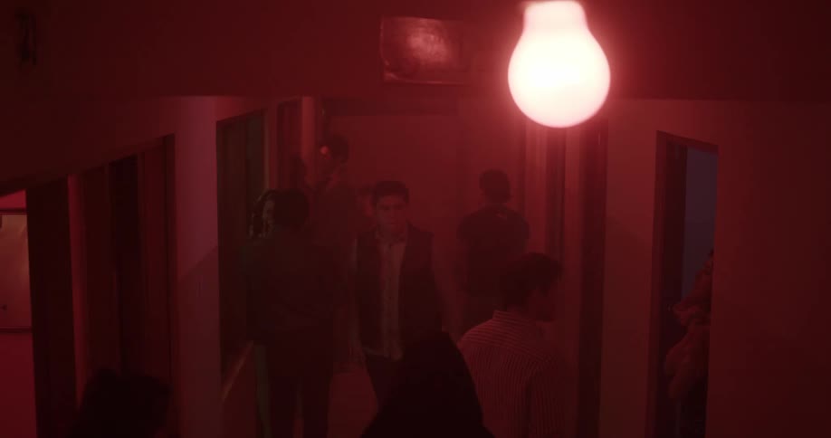 People walk along red tinted corridor under single light bulb