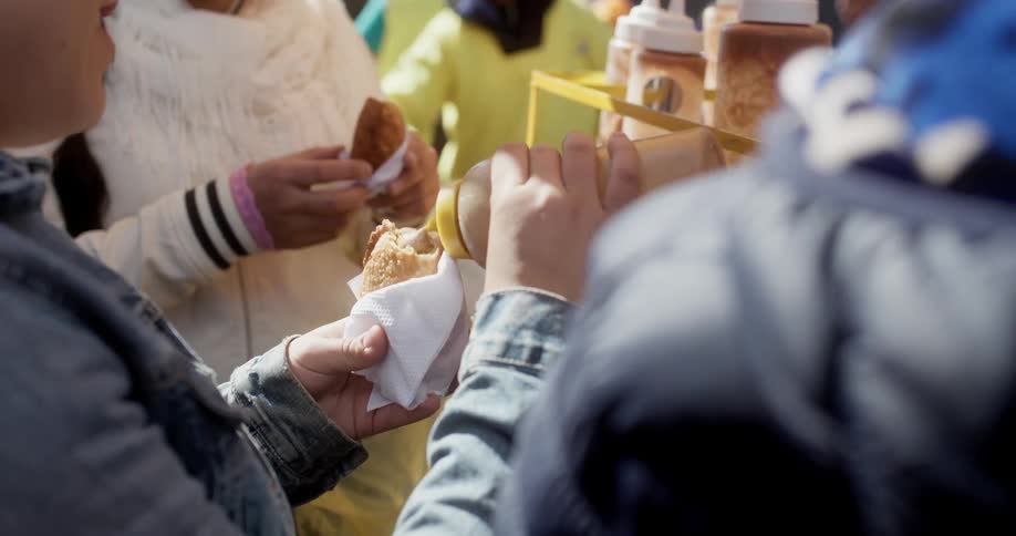 Two women add condiments to their sandwiches in a packed outdoor food bazaar