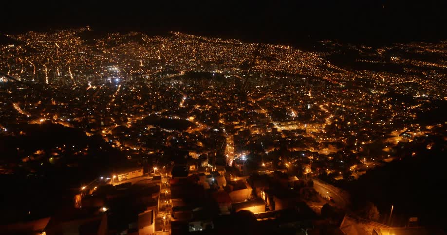 Gondolas going up a hill at night with the lit up city skyline behind them