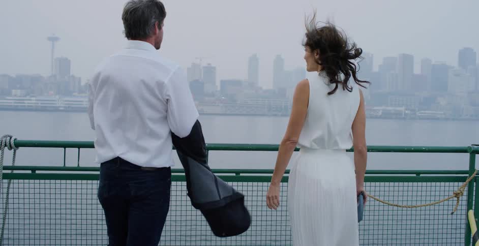 A couple stands on a pier on a cloudy and windy day with a skyline in the background