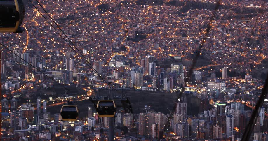 Gondolas moving down a hill in front of a city skyline