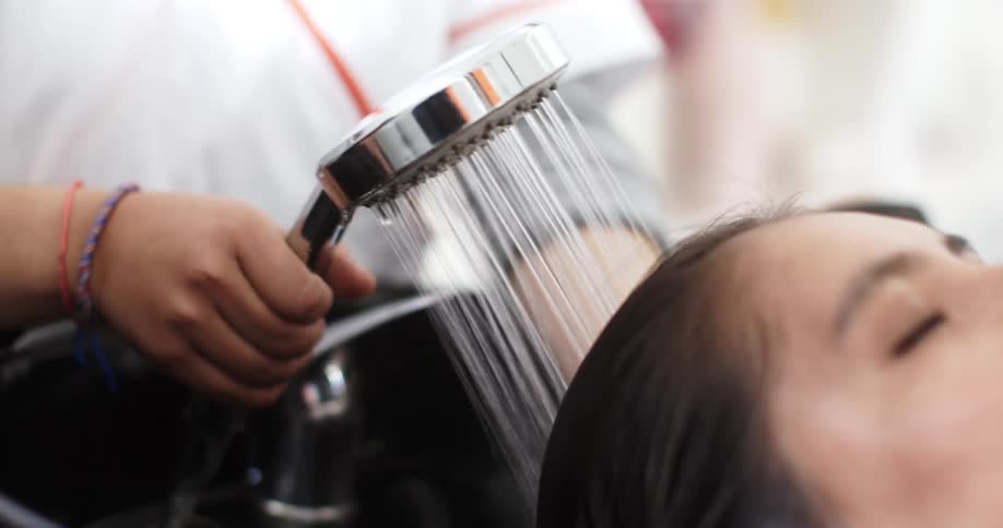 Woman wets another womans hair with a water sprayer in a hair salon
