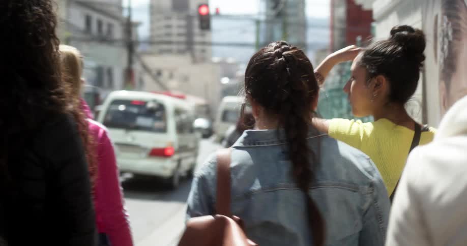 Teenage girls walk down the sidewalk on a busy city street