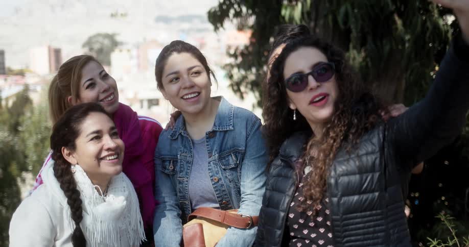 A group of friends make faces and smile as they pose for a selfie with town buildings behind them