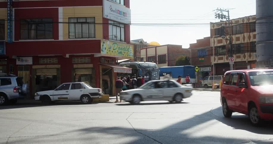 Vehicles driving on a street with people crossing and standing on the corner