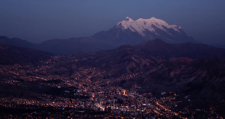 City lights sprawl across valley among low mountains backed by large snow capped mountain