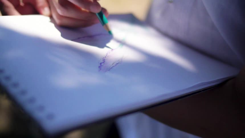 A woman is drawing on paper outdoors