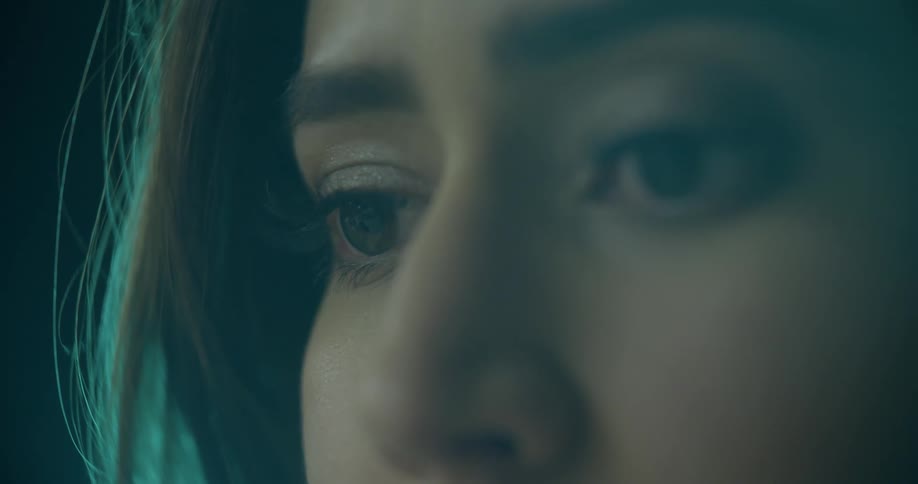 A young woman blinks while a blue light from behind her gives her hair a bluegreen glow