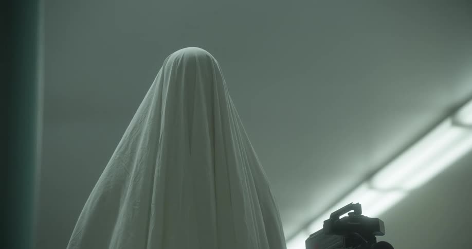 Person standing under white sheet next to recording camera and tv with static