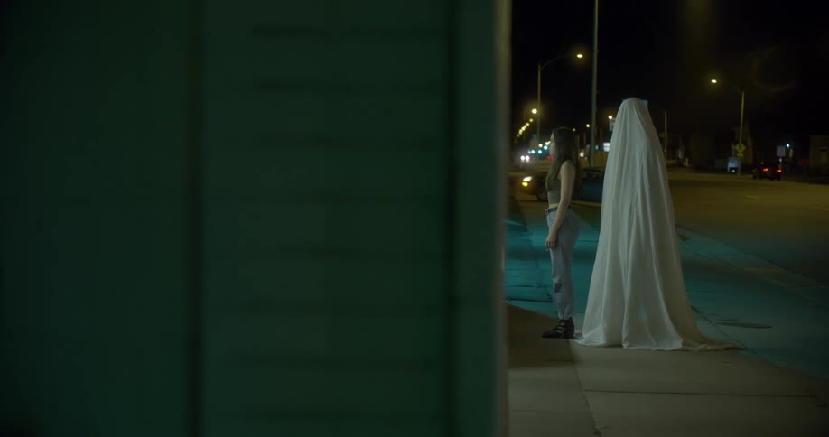 Woman stands near intersection with sheet shrouded person behind her