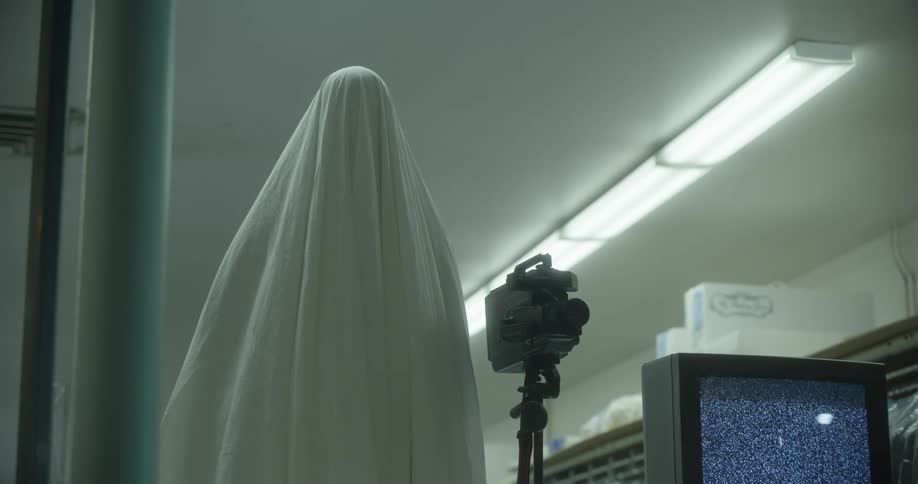 A powered on old television a video camera and a mannequin covered in cloth arranged side by side in a building