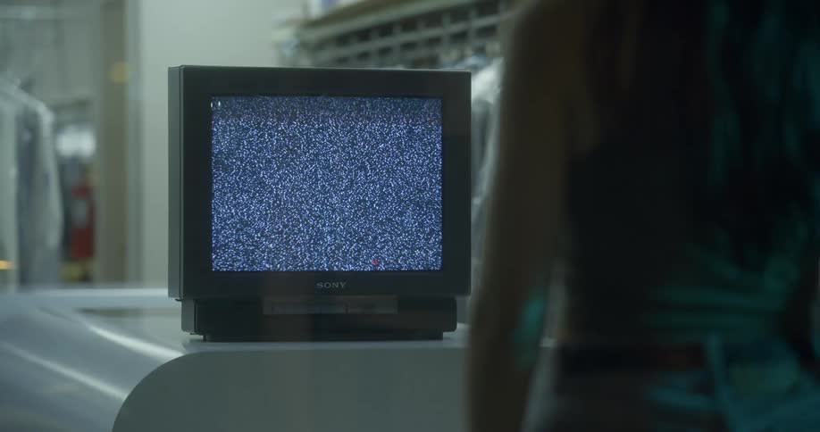 Woman walks toward old television showing static sitting on counter of dry cleaning shop