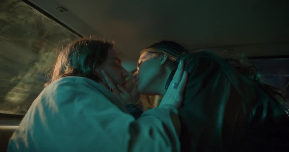 Man with long hair and brunette woman make out in the back of a car at night
