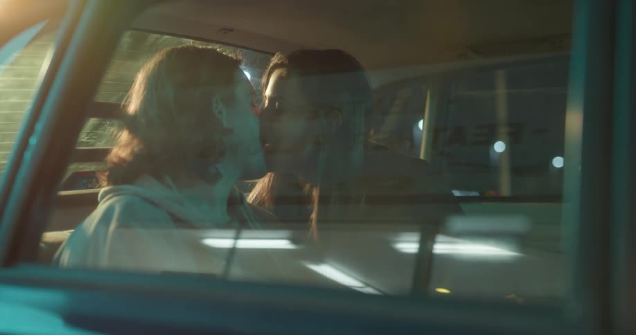 Couple sit in backseat of parked car at night kissing