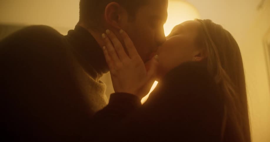 Man and woman kissing besides a lamp in a room at night