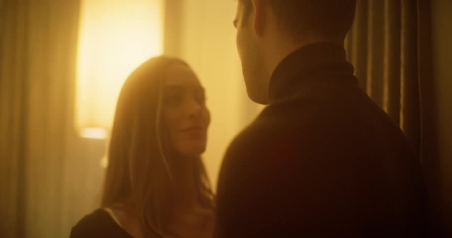 Blonde woman and man with a black turtleneck sweater kiss each other in the bedroom